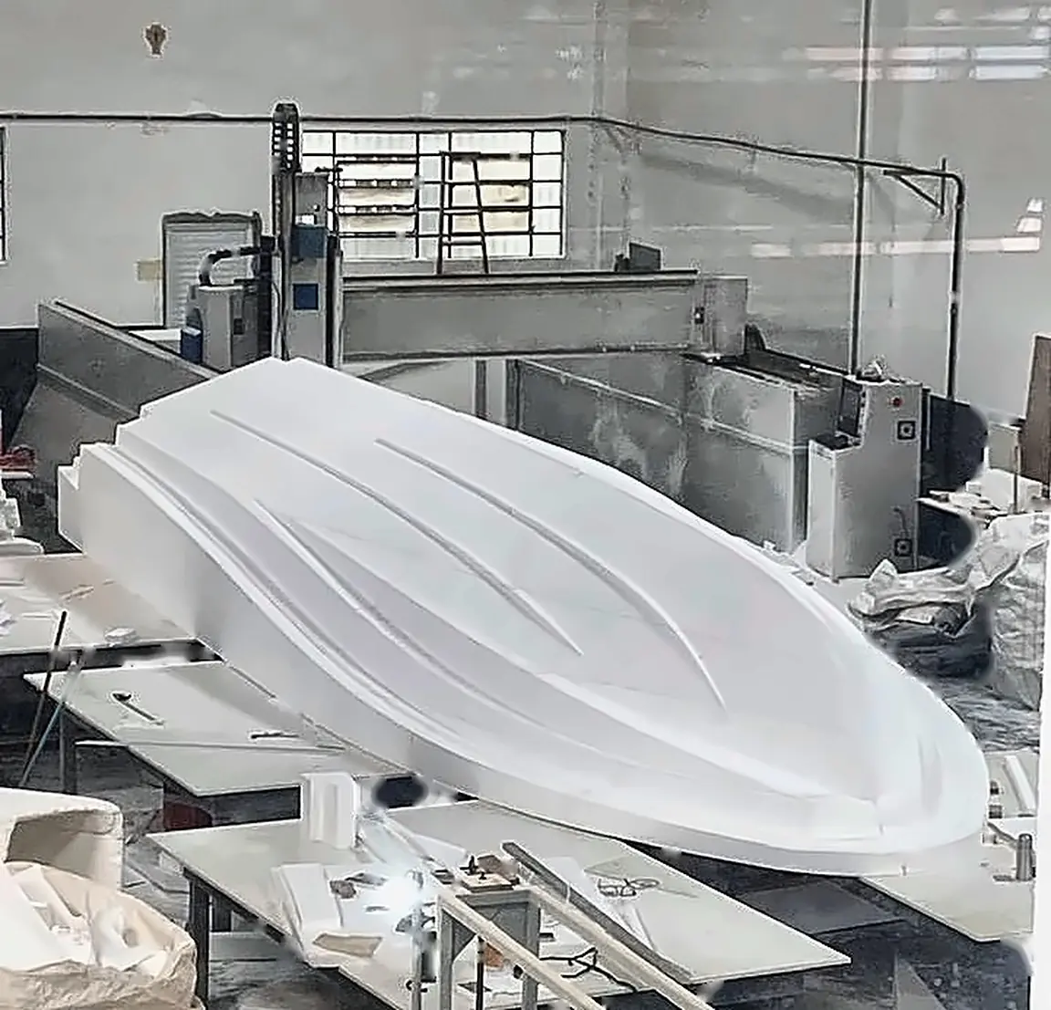 Casco de embarcação em isopor recém-usinado, ao lado da fresadora CNC de pórtico