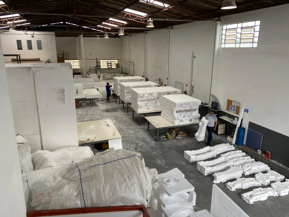 Vista do galpão da Moldtec, com modelos em EPS sobre as bancadas e operadores trabalhando